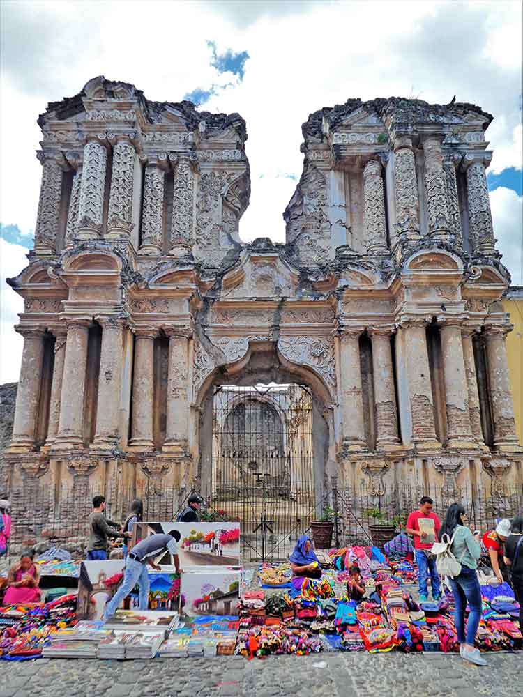 Artisan markets feature goods displayed on the streets, laid out on the floor, with ruins of buildings standing in the background