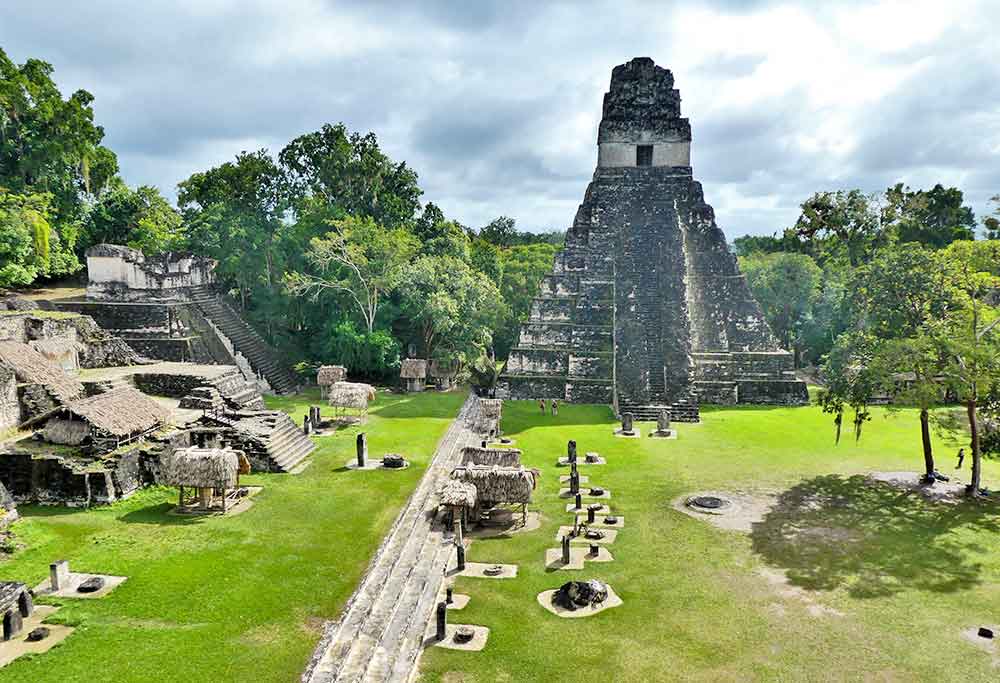 Grand Plaza in Tikal features a large open space surrounded by monumental structure, pyramids and trees
