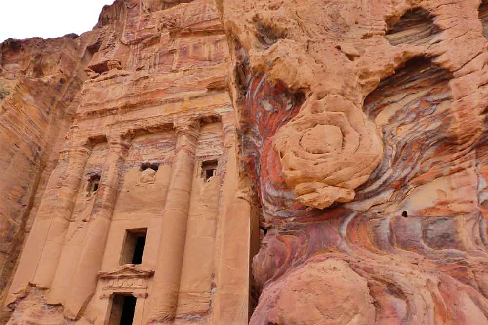 The Urn Tomb at Petra features carved columns and high rock formations in a sand-colored hue.
