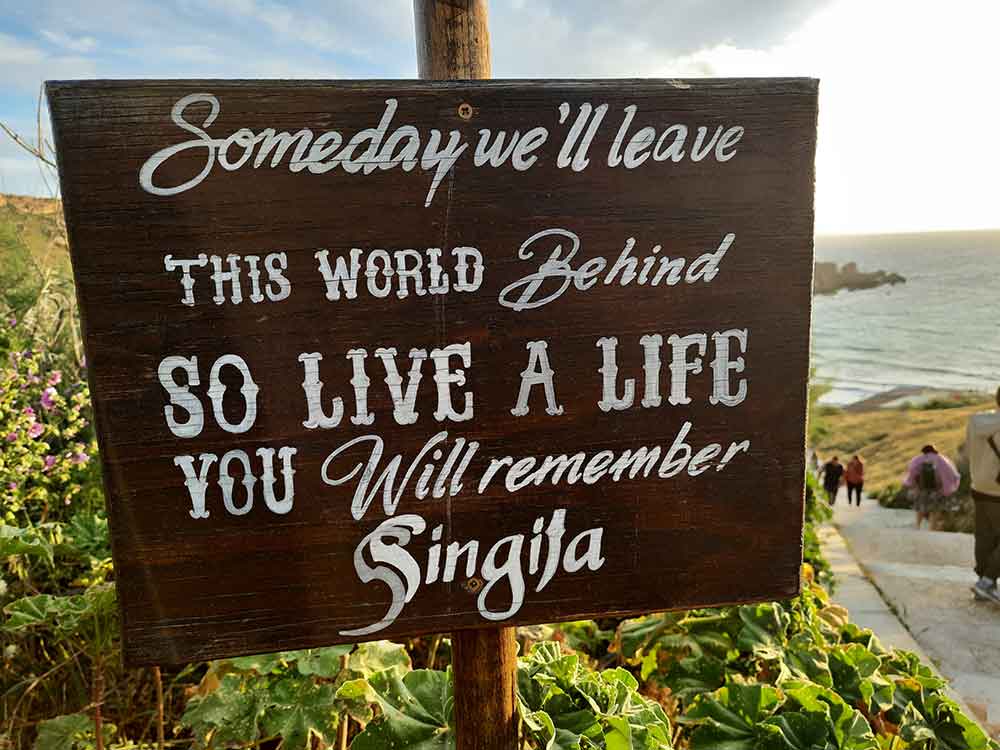 A brown board sign with a message of "Someday we'll leave this world behind so live a life you will remember Singila"