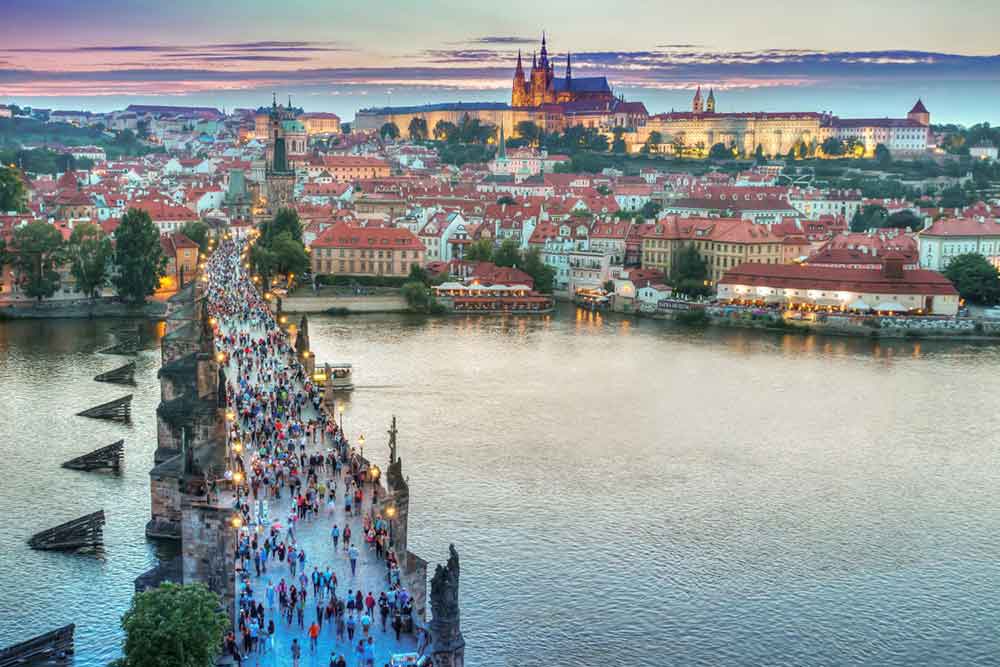Charles Bridge in Prague with lots of pedestians walking on in at sunset.