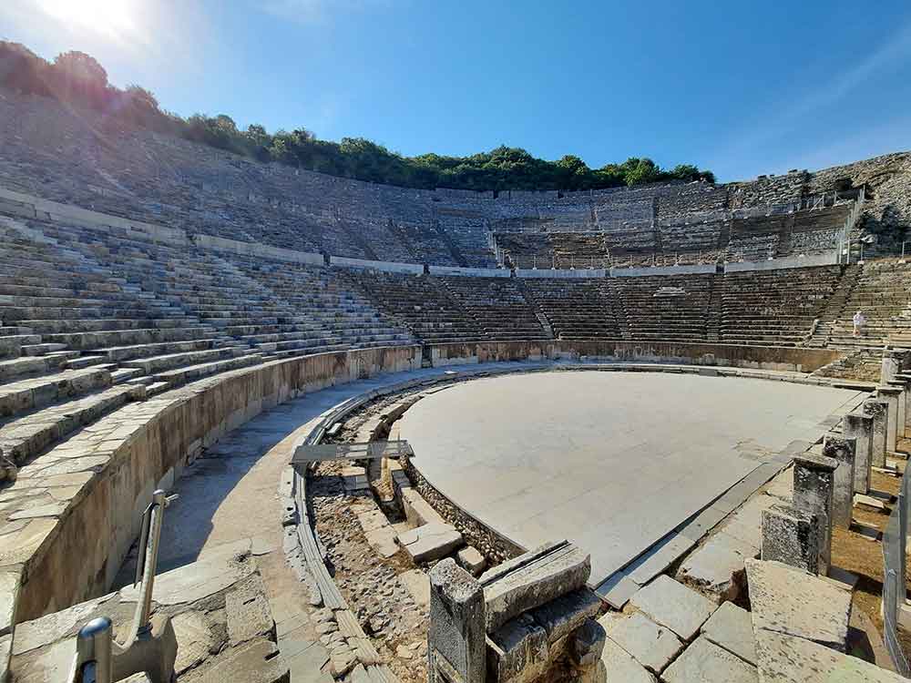 A large semi-circular amphitheatre at the ruins of Ephesus. There is blue sky and sunshine. 