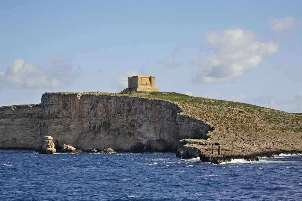 One Week in Malta: The Best 7 Days in Malta Itinerary 25 Comino Island features rugged cliffs alongside a beautiful blue beach on a sunny day