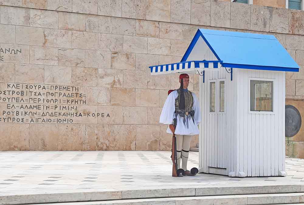 The Presidential Guard, dressed in their traditional uniforms, is standing beside a small house with a white and blue roof