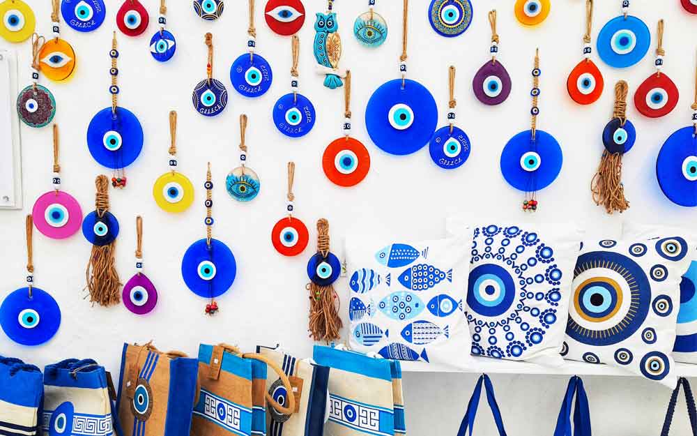 Vibrant blue and red crafts, bags, and pillows are displayed in shops in Mykonos
