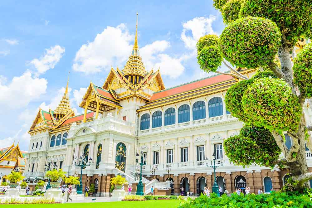 The beautiful Grand Palace in Bangkok showcases its gold and red roof, with a majestic tree standing beside it