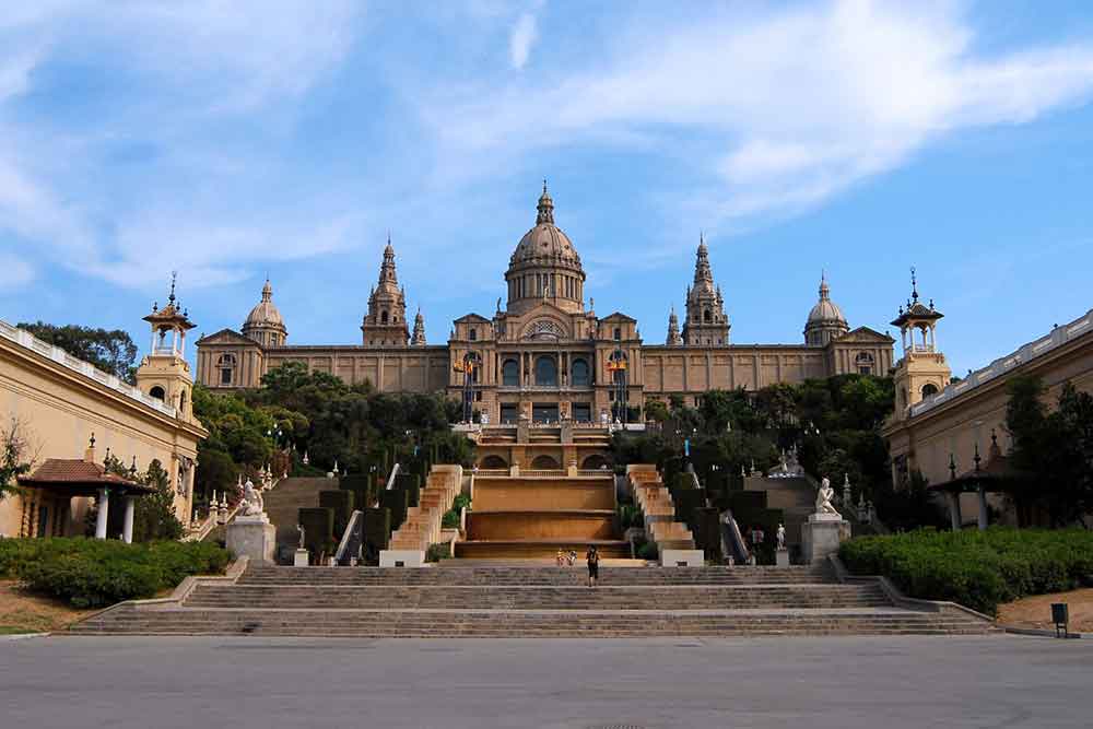Barcelona Bucket List: 32 Best Things to Do in Barcelona, Spain 13 The Museu Nacional d'Art de Catalunya features a staircase going up, surrounded by trees, under a clear blue sky