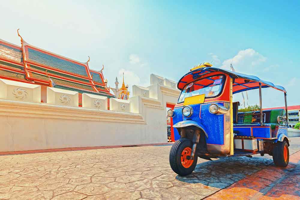 A Tuk Tuk, a three-wheeled transportation vehicle, with a red and blue color combination, is parked at the Grand Palace in Bangkok