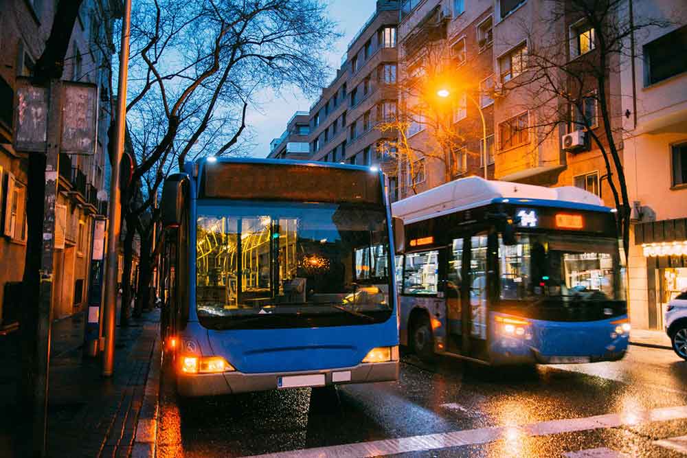 Two blue buses are driving down the streets of Madrid 