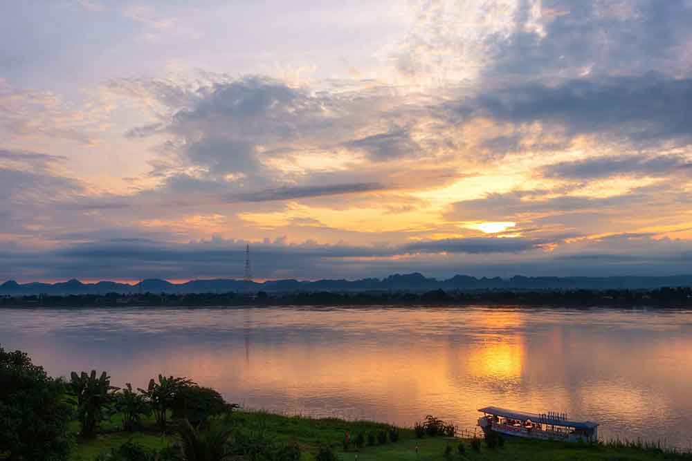 A serene morning atmosphere at Mekong River, with aboat gently gliding along while offering a view of majestic mountains on the background