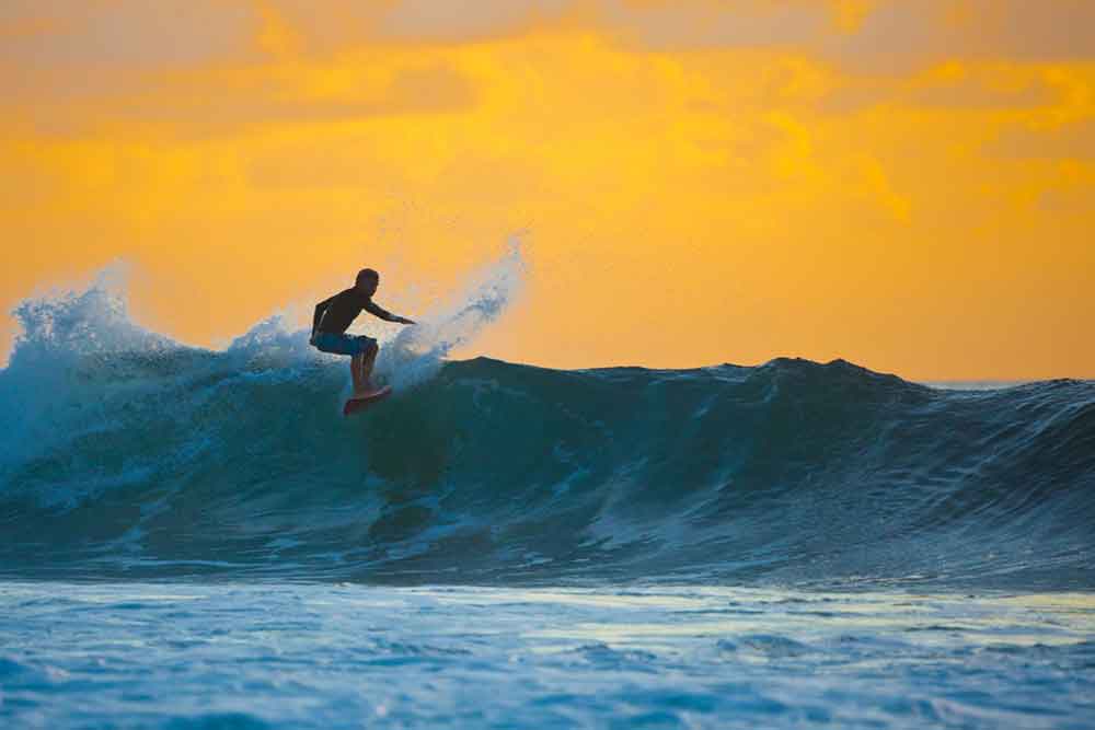 A surfer rides a wave at sunset in Bali