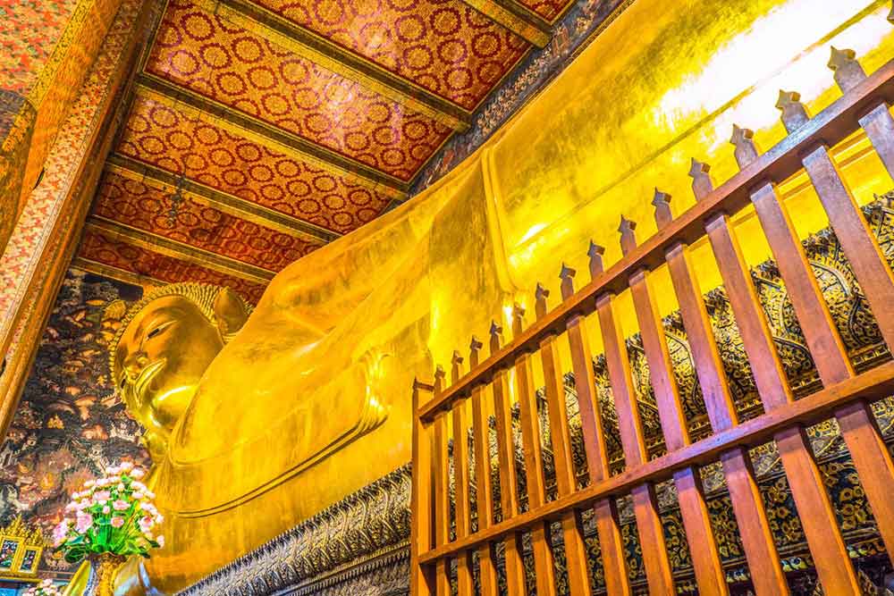 The Golden Reclining Buddha at Wat Pho features Buddha lying on his side, with his hand supporting his head, inside a temple 
