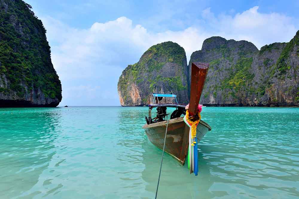 A long-tail boat is positioned in the middle of Maya Bay beach, surrounded by its turquoise waters and towering cliffs