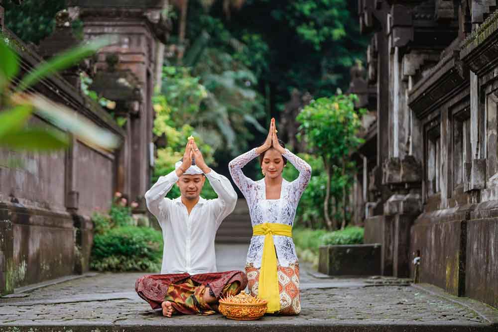 Two hindu people sitting on the ground making an offering to their God in Bali