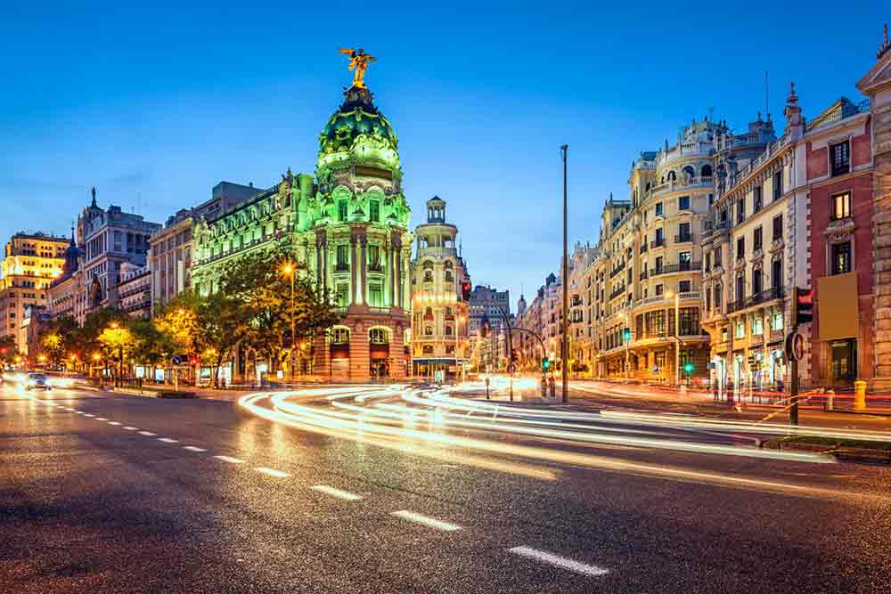 Gran Via in Madrid, Spain, lined with busy streets and colorful, lighted buildings, with a clear blue sky in the background