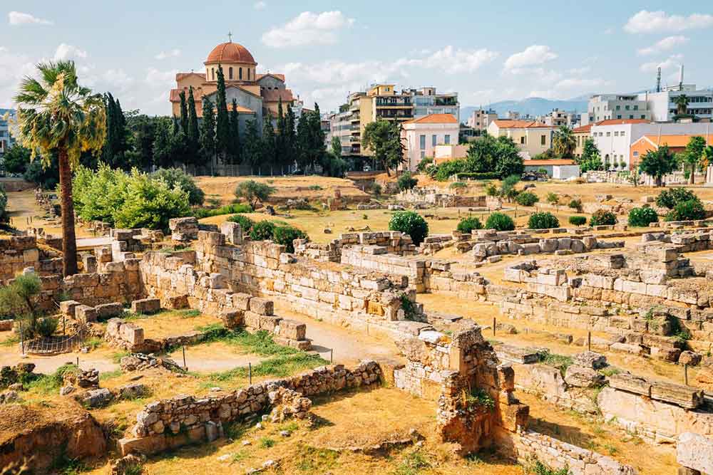 Kerameikos Cemetery with its ancient yellow gold bricks and stones, accompanied by the presence of lush plants and trees with houses on the background on a sunny day 