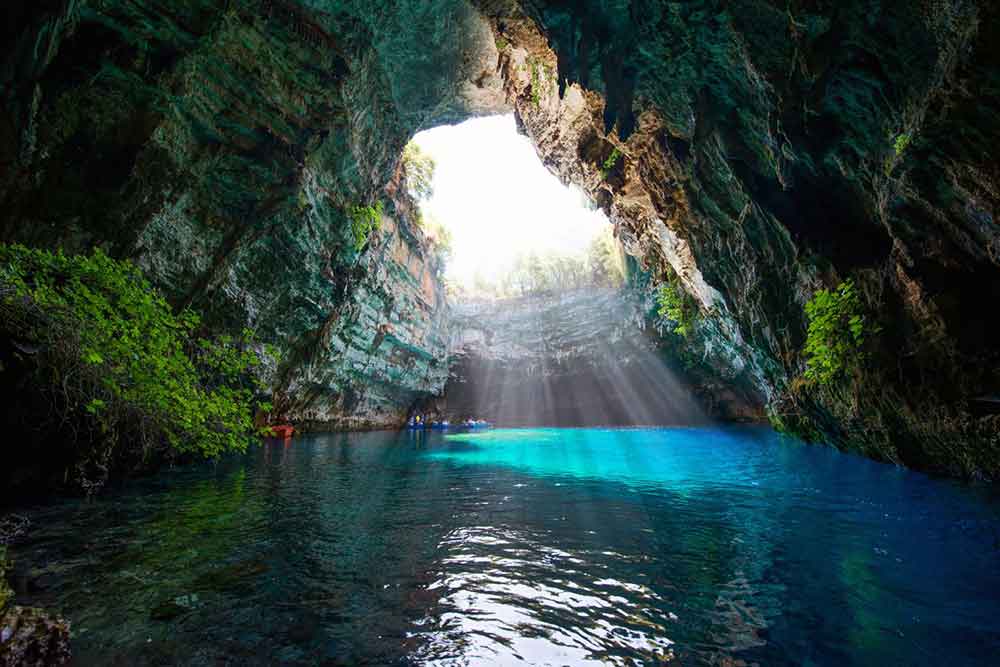 Melissani lake surrounded by natural rock formations with a play of sunlight in the middle
