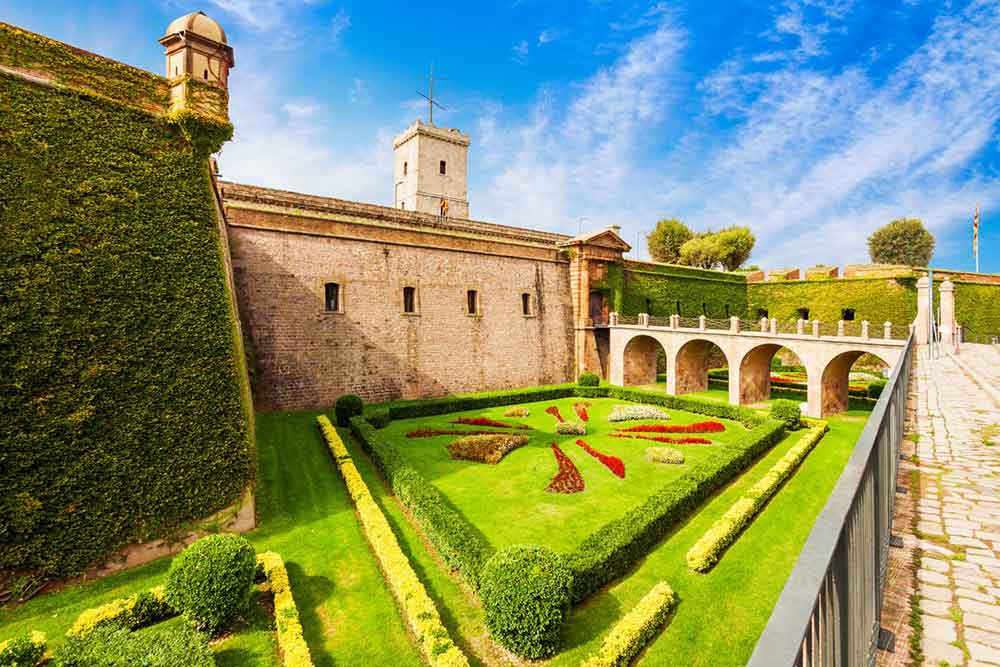 Barcelona Bucket List: 32 Best Things to Do in Barcelona, Spain 19 Well-manicured garden in Montjuïc Castle features lush green plants and trees, all under a blue sky