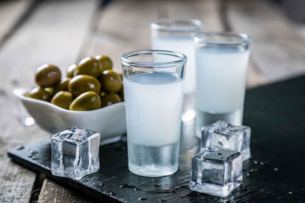Ouzo in three shot glasses with appetizers and ice