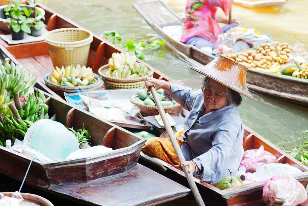 The woman vendor is selling her goods at the Damnoen Saduak Floating Market, sailing along the water