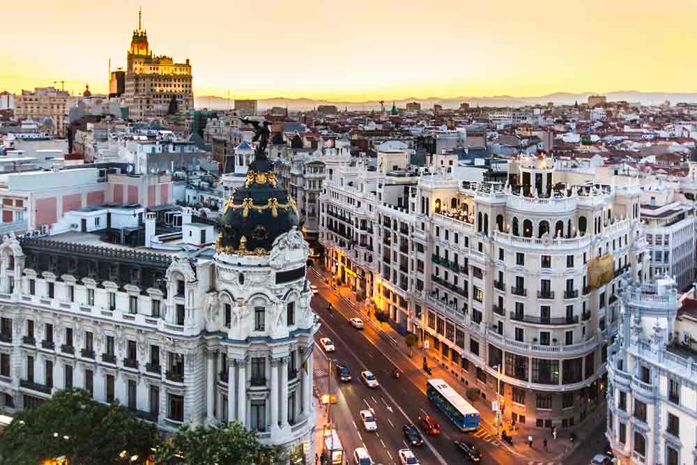 View of Gran Via cityscape with the Metropolis building, houses, apartments, and cars in Madrid at sunset time