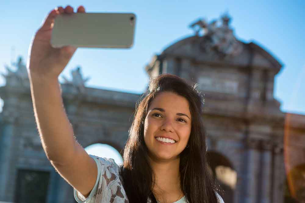Young woman tourist taking a selfie with her phone in Alcala Gate of Madrid
