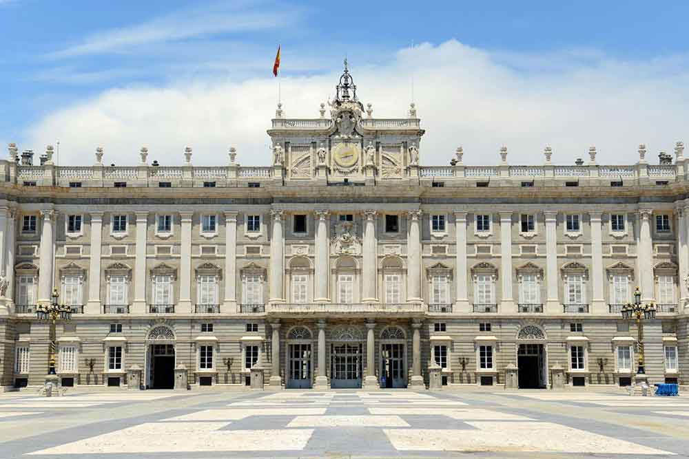 El Palacio Real in a cream-colored stone with a symmetrical and decorative design with a blue cloudy sky on the background