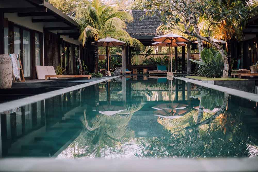 Affordable luxurious villa in Bali with house, large pool, lounge chairs and umbrellas 