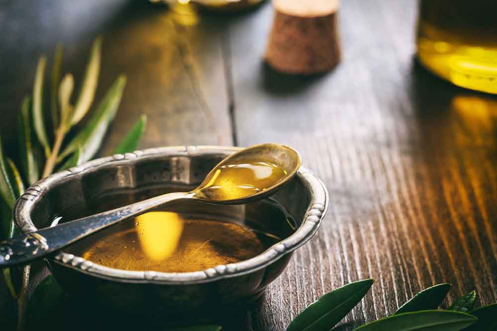 Greek olive oil in a bowl and spoon with olive leaves on the side