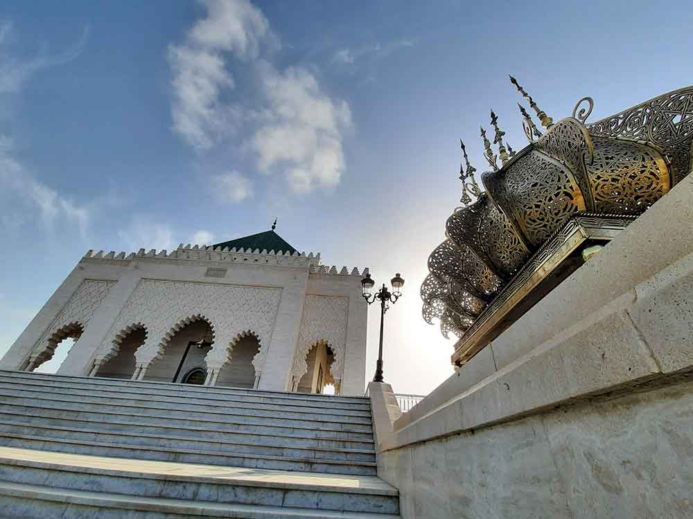 The Mausoleum of Mohammed V in Rabat covered with white marble and a pyramidal green roof in a clear blue sky 