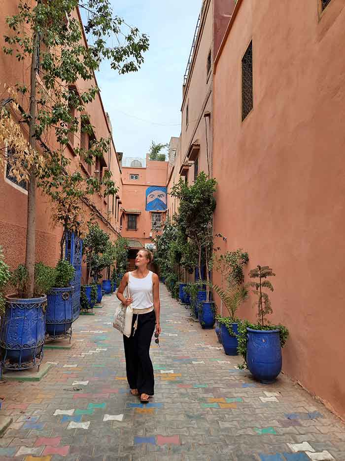 Woman (Becki from Meet Me In Departures) walking through a narrow alley in Marrakech with a tote bag and holiday essentials