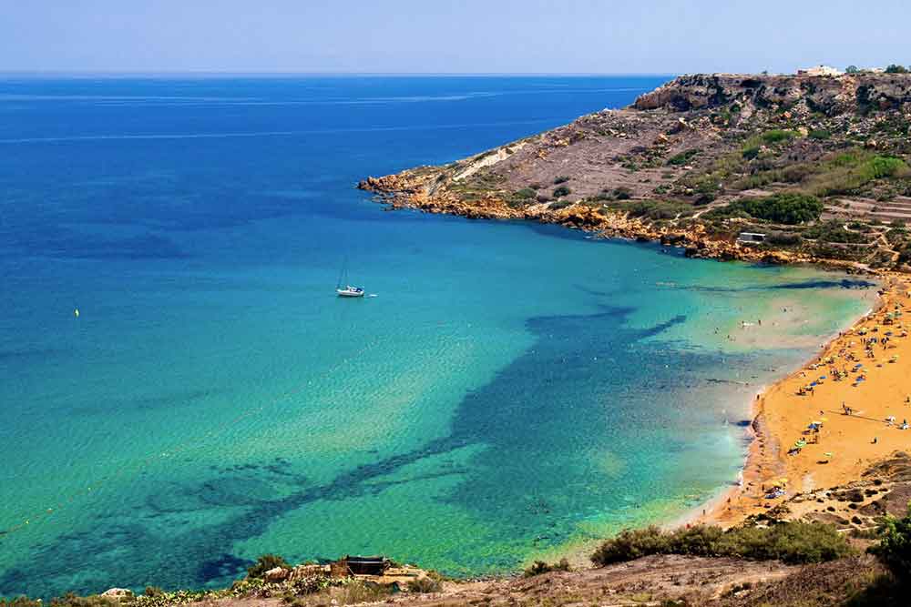 Crystal clear blue water with a boat surrounded by a mountain on the side at Ramla Bay