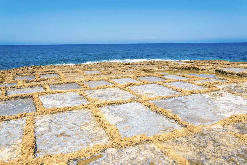 A Salt Pans  - a shallow rock-cut pools with a geometric patterns filled with sea water in a sunny day
