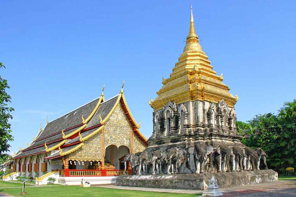 How to Spend a Month in Thailand: Best 1 Month in Thailand Itinerary 15 A temple with a three-tiered roof, decorated with carvings in gold and ochre colors, stands beside a statue of a standing group of elephant adorned with gold on top of it