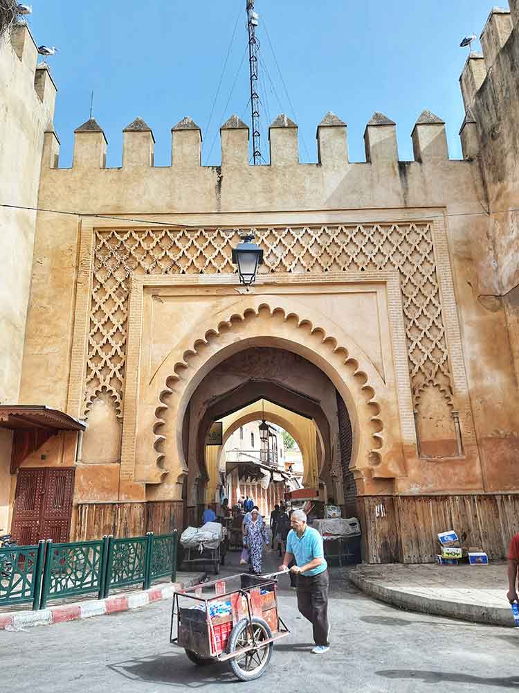 A man with a cart stands in the gateway of Fes, framed by intricate white-brown walls.
