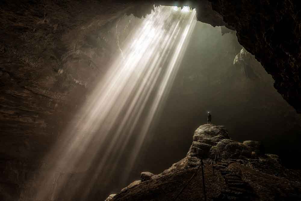 Goa Jomblang Cave in Java, Indonesia surrounded by rock formations with a dazzling beam of sunlight that shines through the cave's opening