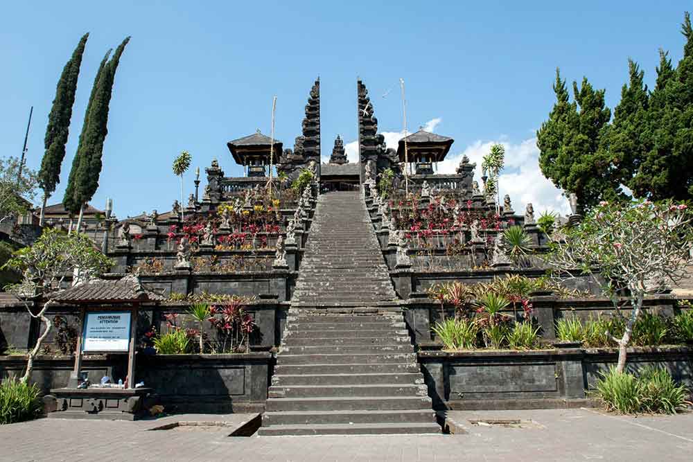 Besakih Temple in Bali with a grand stone staircase, lined with plants and statues in a clear blue sky