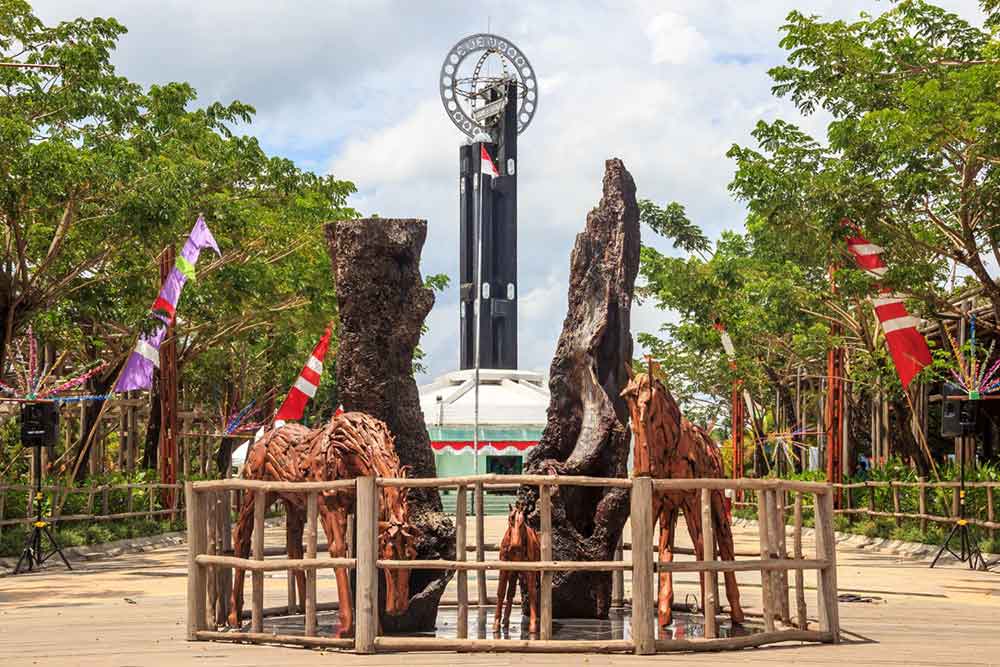 Equator Monument, Pontianak - a tall obelisk topped with a globe surrounded by trees and wooden horses at the middle