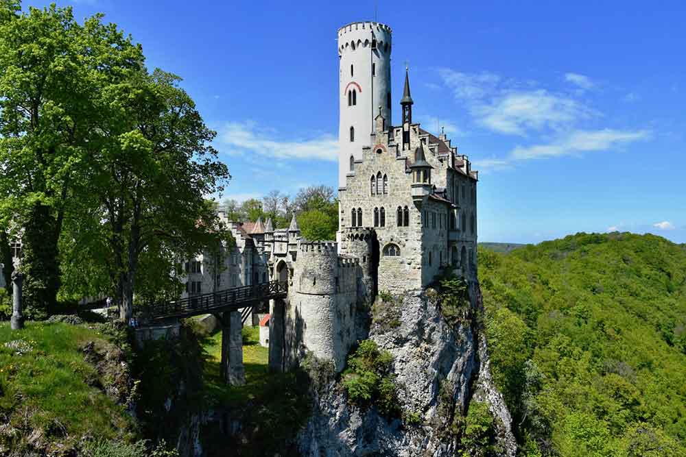Lichtenstein Castle in Germany features a fairy tale like castle perched atop a rocky cliff with its tall, slender towers, pointed arches and gray-painted wall