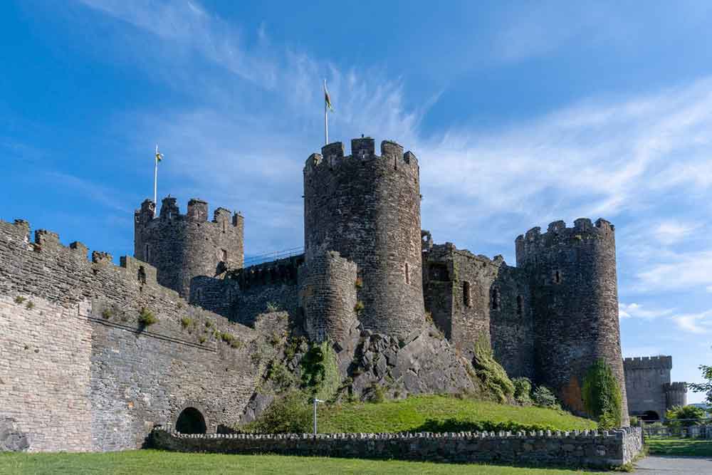 Conwy Castle in Wales features massive stone walls and towers resembling a rook, all under a blue sky in the background
