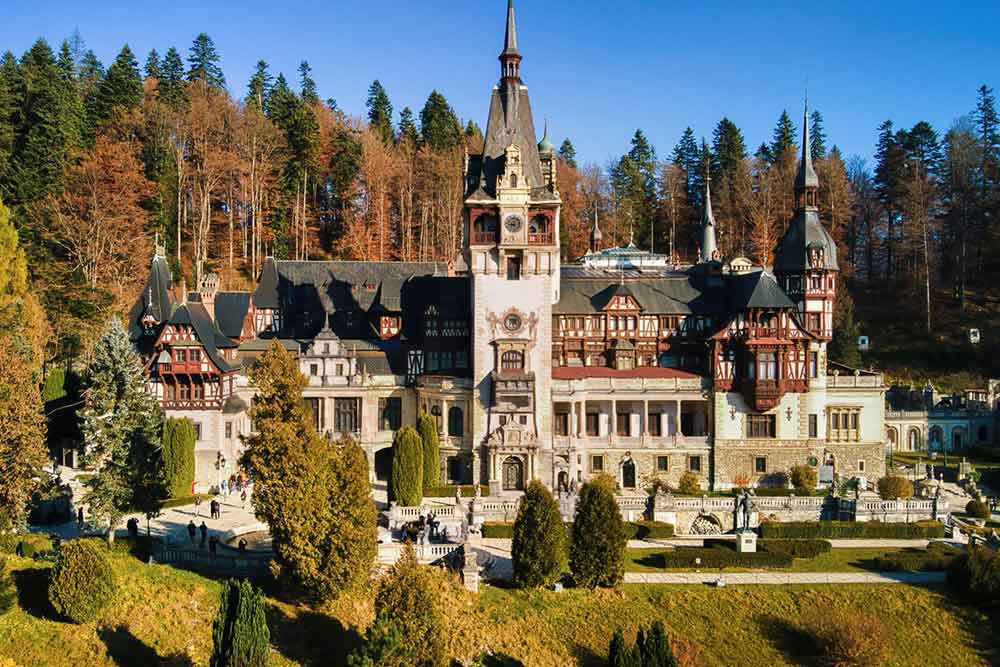 Peles Castle in Romania is a fairytale-like palace nestled in a lush forested landscape - showcases towers, turrets, spires, red walls, and intricate windows