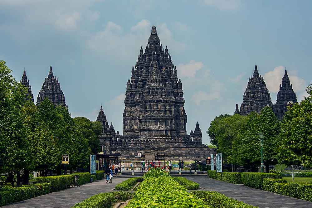 Prambanan Temple in Java, Indonesia showcases the towering temples with intricate volcanic  stone carvings and sculptures, set amidst a lush environment of trees and plants