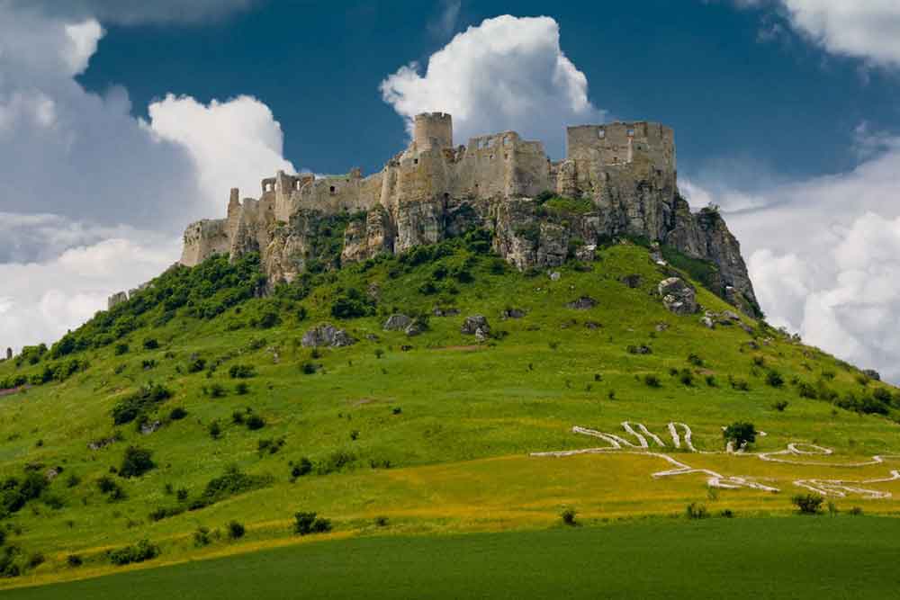 Spis Castle in Slovakia stands atop a limestone hill, with its towering stone walls and fortified towers, all surrounded by lush green land