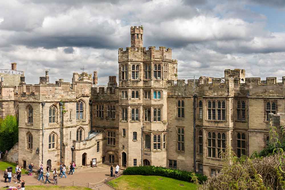 Warwick Castle in England features sandstone walls and battlements, along with multiple windows, attracting numerous tourists