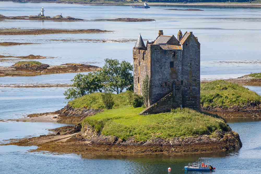 Castle Stalker in Scotland showcases a tower crowned by a conical roof, while its walls are adorned with small windows, primarily built in grey stone
