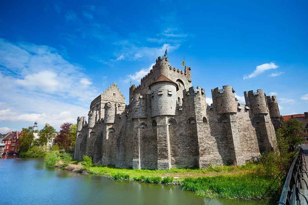 Castle of Gravensteen stands tall in Belgium, showcases a formidable structure made of stone, with high walls, sturdy towers, and battlements surrounded by lake
