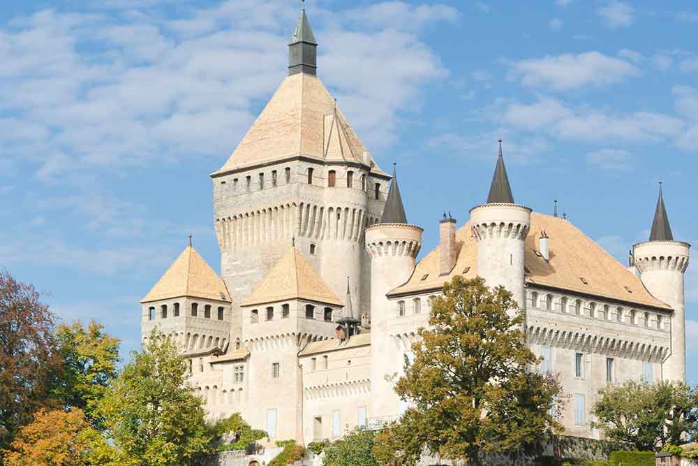 Vufflens Castle, Switzerland with its multiple brown turrets and high towers surrounded by trees