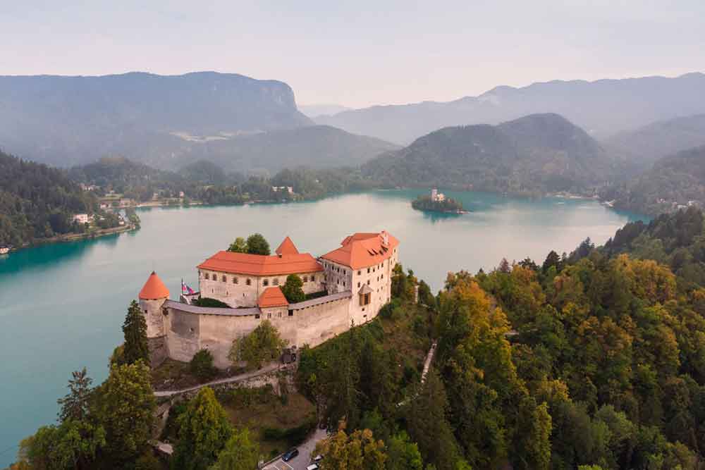 Lake Bled Castle in Slovenia with its red-roof and cream high walls standing atop a rocky cliff overlooking the stunning Lake Bled 