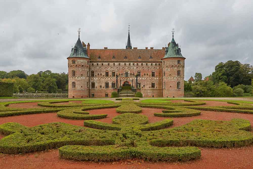 Egeskov Slot, Denmark features a red-brick walls, red roofs with blue turrets surrounded by expansive gardens and manicured lawns