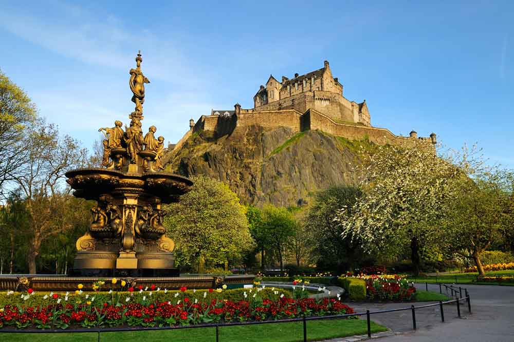 Edinburgh Castle is situated atop Castle Rock in Scotland, featuring a statue and garden at the entrance